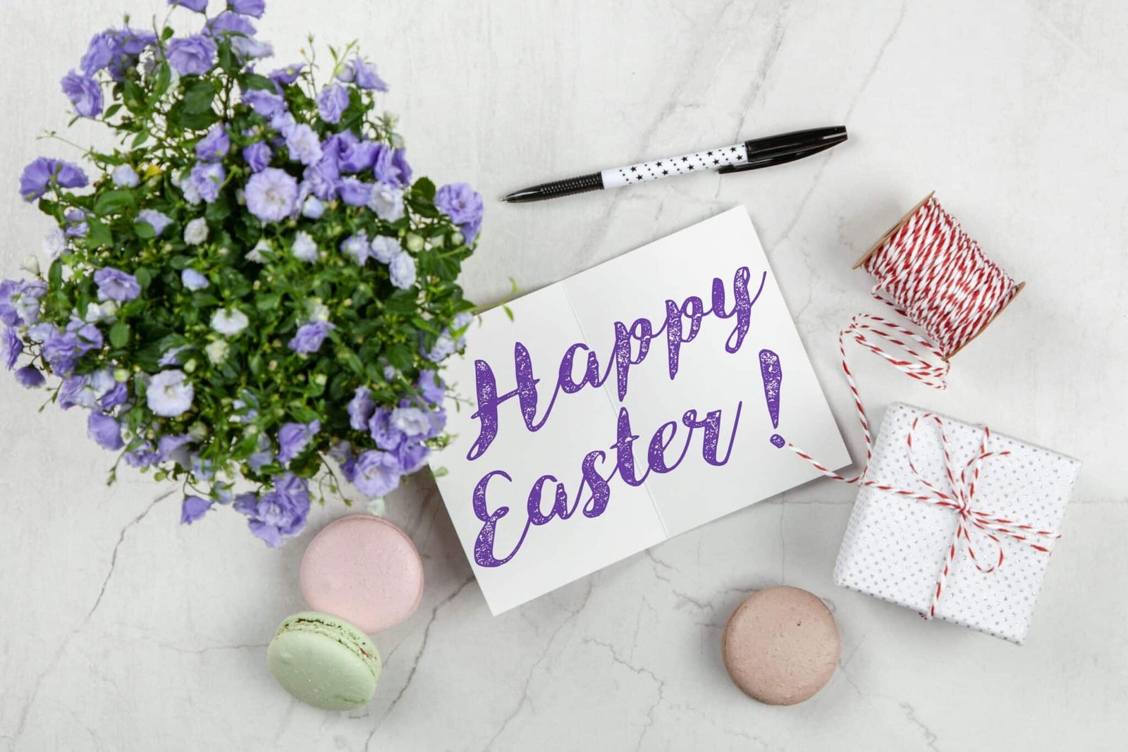 Easter greeting card with flowers, macarons, and gift on a marble surface.