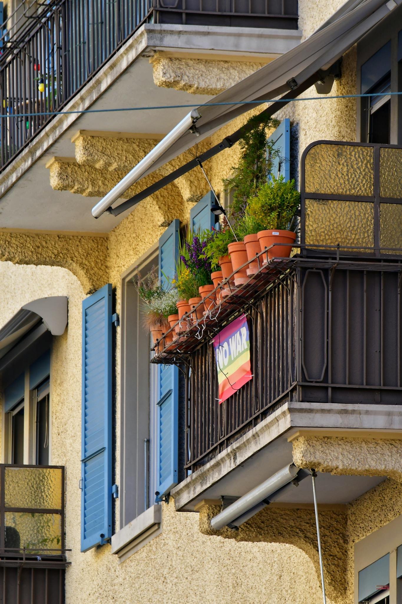 A vibrant urban balcony with plants and a rainbow 'No War' sign adds charm to the building facade.
